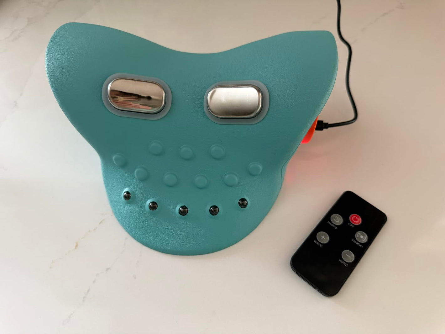 Turquoise back massager with two silver buttons and a remote control on a white surface.