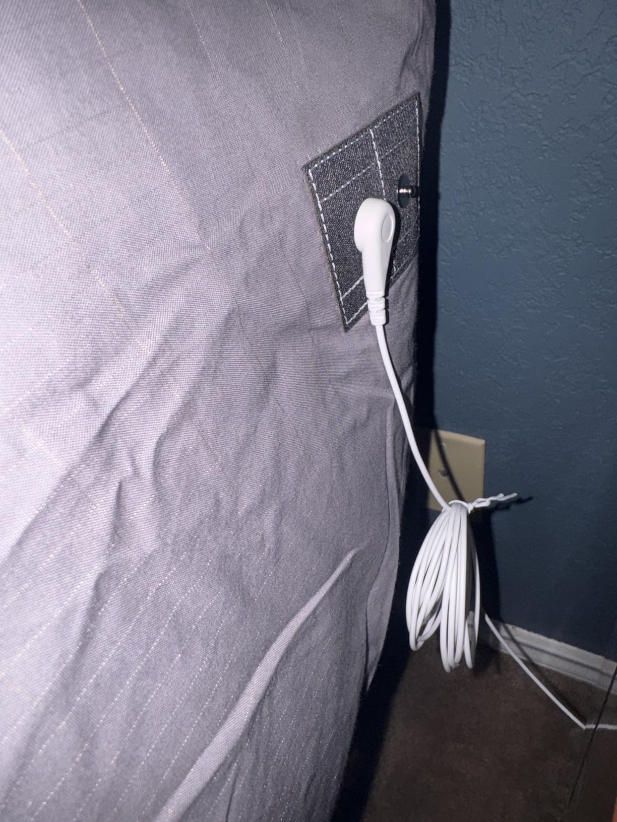 White cable plugged into a wall socket on a gray wall.