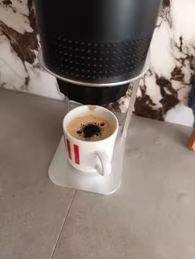 Coffee being poured into a white mug with red stripes on a marble countertop.